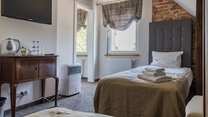 Un dormitorio con cama, cómoda, radiador, televisor y ventana con cortinas.