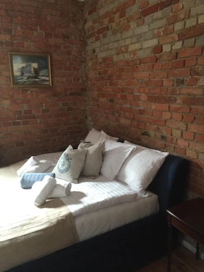 A room with a brick wall, a bed with white bedding and multiple pillows, and a framed picture on the wall. - Villa Italiana (Gdynia)