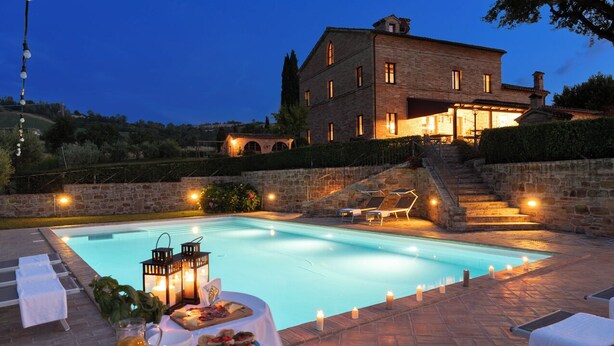 A poolside dining area with a table set for two, a stone wall, and a building in the background.