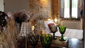 A room with a brick wall, a window with curtains, and a table with glassware and flowers.