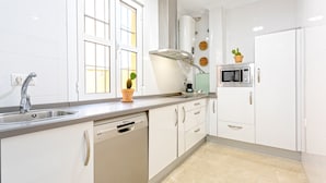 Una cocina moderna con armarios blancos, lavavajillas, microondas y una ventana con persianas.