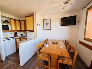 A compact kitchen with wooden cabinets, a microwave, a refrigerator, and a dining area with a wooden table and chairs.
