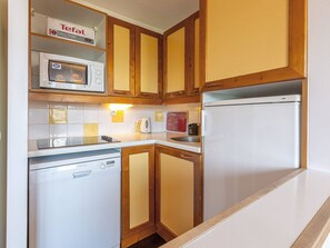 A compact kitchen with wooden cabinets, a microwave, a dishwasher, and a refrigerator.