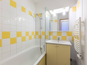 Un baño con una bañera blanca, un revestimiento de pared amarillo y blanco, un espejo y un lavabo blanco con armario.
