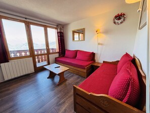 Una habitación acogedora con piso de madera, un sofá rojo, una cama de madera, una mesita y una ventana con vistas.