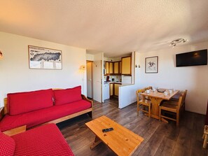 Un espace de vie compact comprenant un canapé rouge, une table à manger en bois et un coin cuisine.