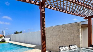 A covered outdoor area with a pool, a table with chairs, and a stone wall. - Located only minutes away from the Palm Beaches. 2 bedroom 3 beds 2 bathroom (Noord)