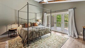 A four-poster bed in a room with a large window and a view of greenery outside.