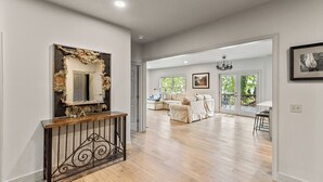 A spacious living room with a wooden floor, a large mirror with a decorative frame, and a dining area with a bar stool.