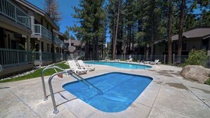A swimming pool with lounge chairs, surrounded by a building with balconies and trees. - Clean Mountain Getaway! Excellent location in Mammoth w/full renovation (Mammoth Lakes)