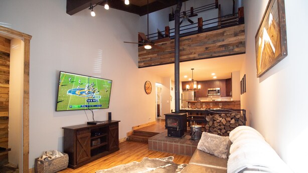 A spacious living room with a large flat-screen TV, a wooden ceiling, a fireplace, and a cozy seating area with a fur rug. - Clean Mountain Getaway! Excellent location in Mammoth w/full renovation (Mammoth Lakes)