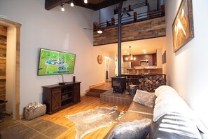 A spacious living room with a large flat-screen TV, a wooden ceiling, a fireplace, and a cozy seating area with a fur rug. - Clean Mountain Getaway! Excellent location in Mammoth w/full renovation (Mammoth Lakes)