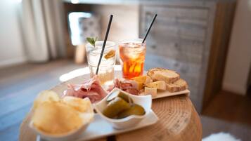 Taula de fusta amb diverses menes d'aliments, com formatge, carns i pickles, acompanyats per dues begudes amb canuts.
