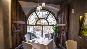 A dining area with a rustic wooden interior, a large arched window, and a table set for two. - La Filanda Relax & Gourmet (Denno)