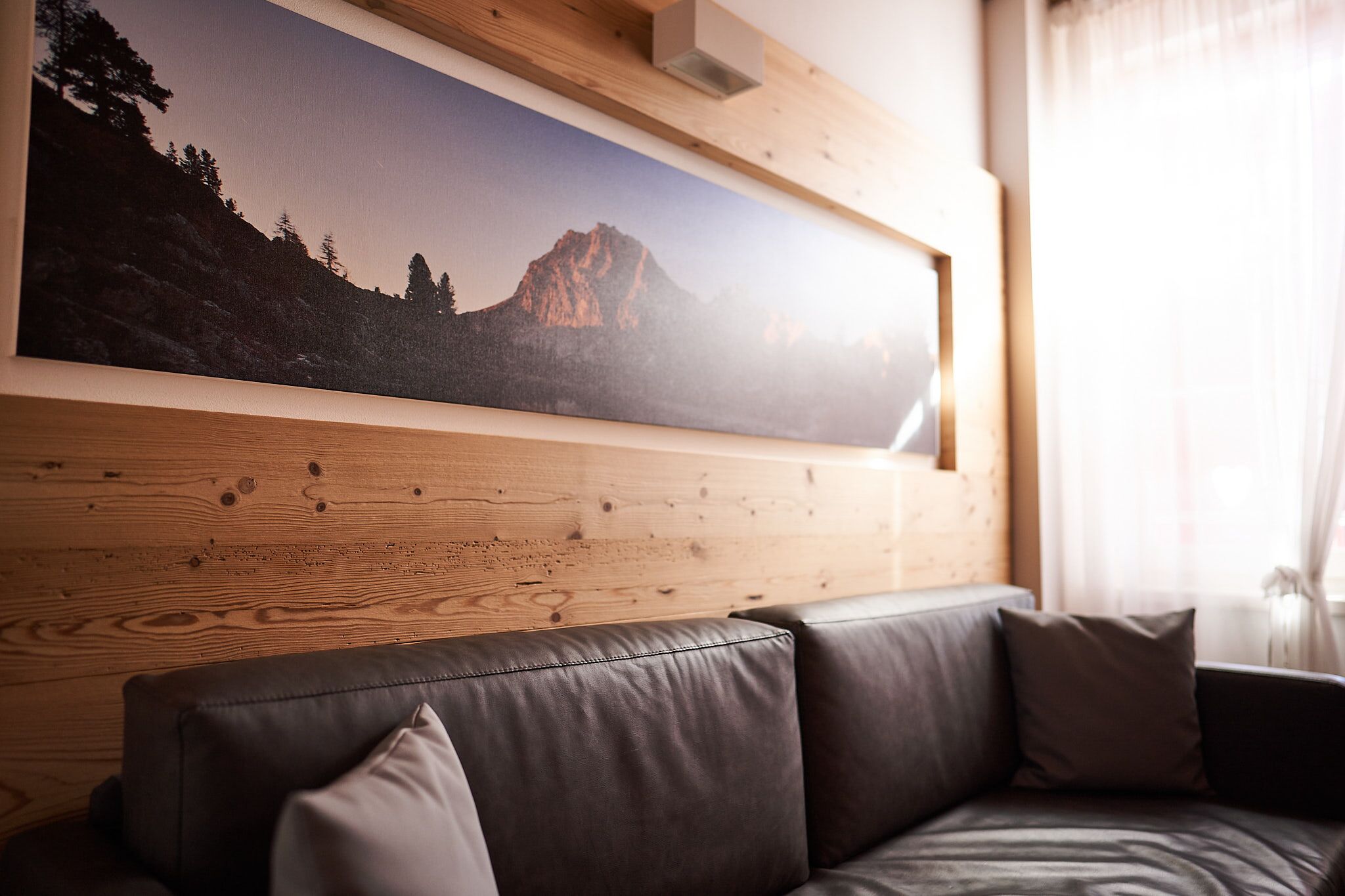 A wooden wall with a framed landscape painting and a leather sofa with cushions.