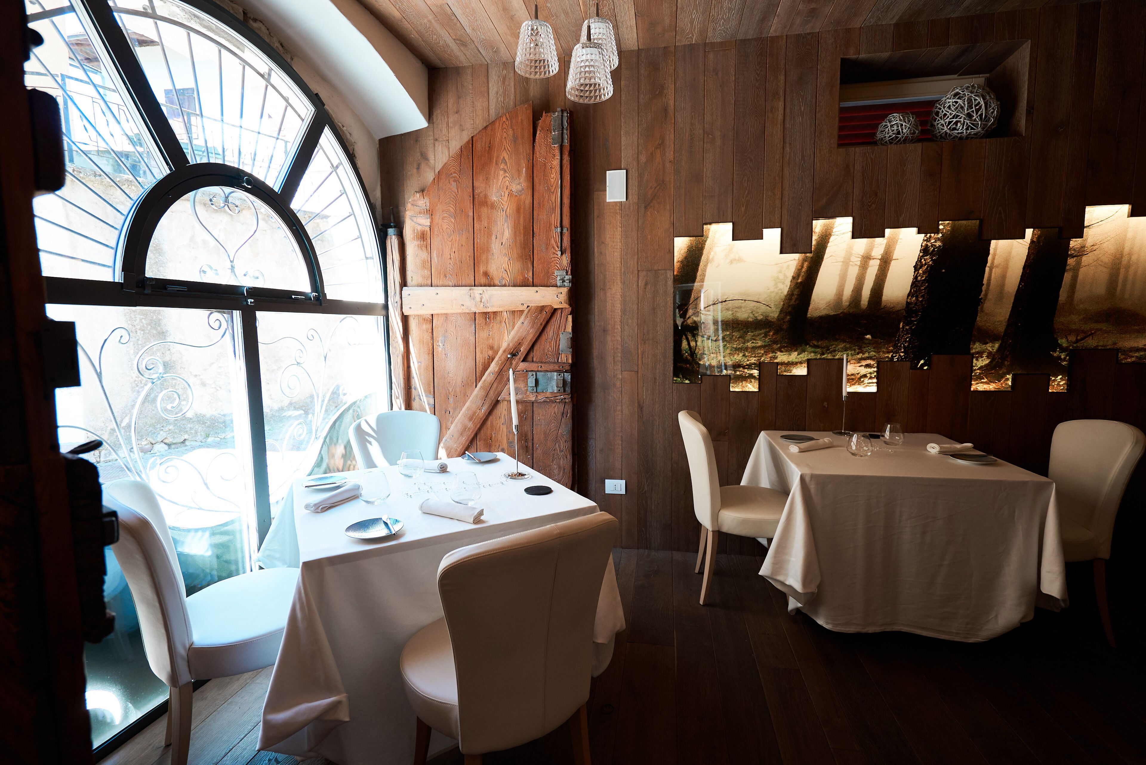 A dining area with a large window, wooden walls, and a table set for two.