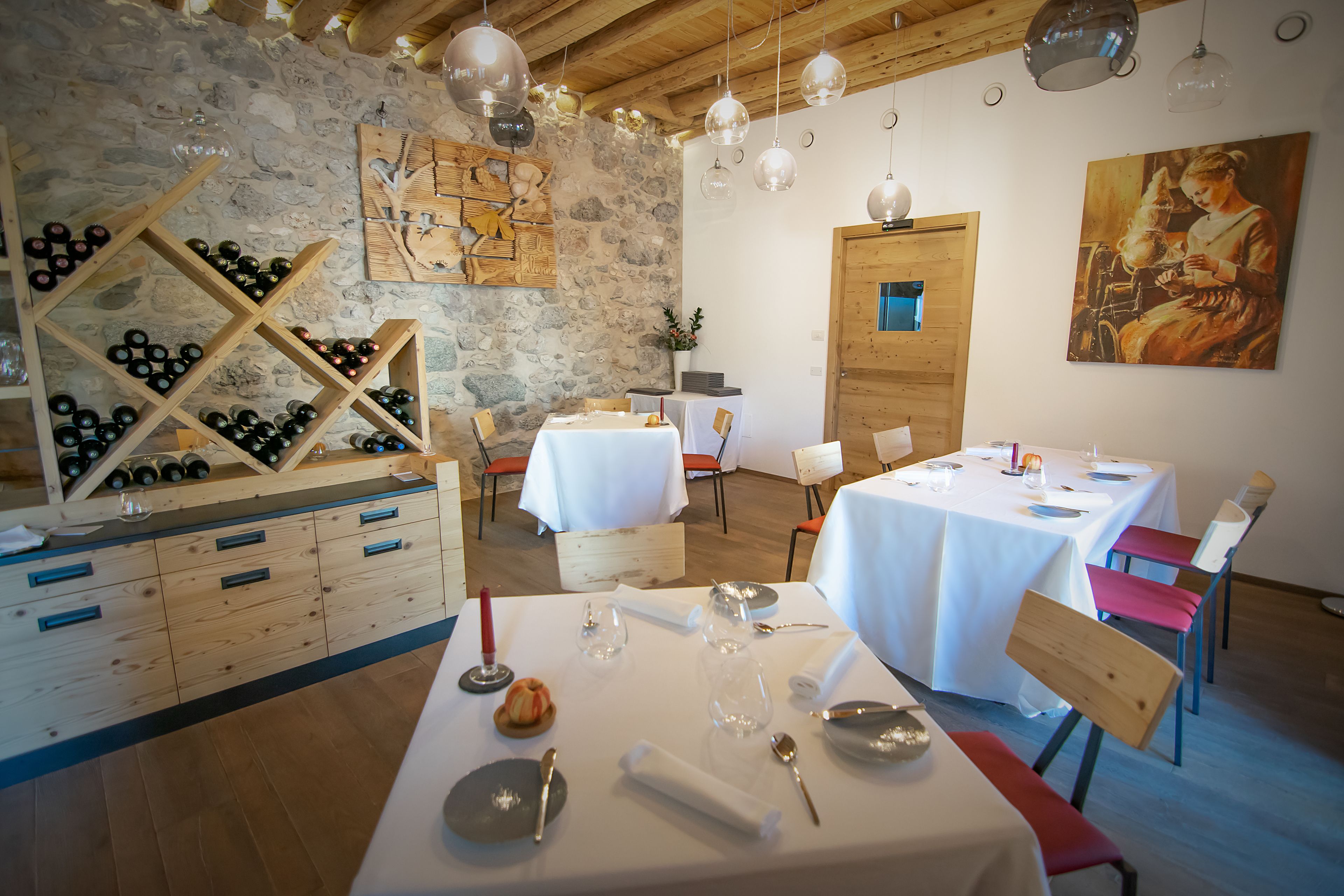 A restaurant with wooden tables and chairs, a wine rack, and a painting on the wall.