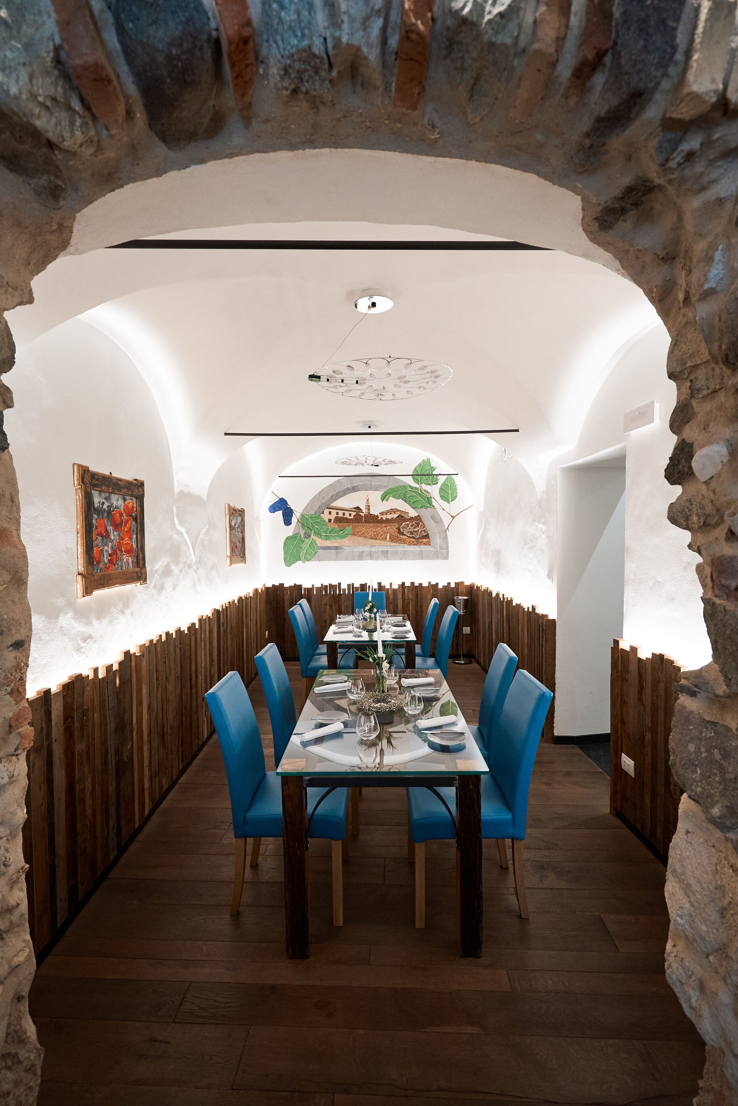 Um restaurante com uma longa mesa de madeira, cadeiras azuis e uma parede rústica de pedra.