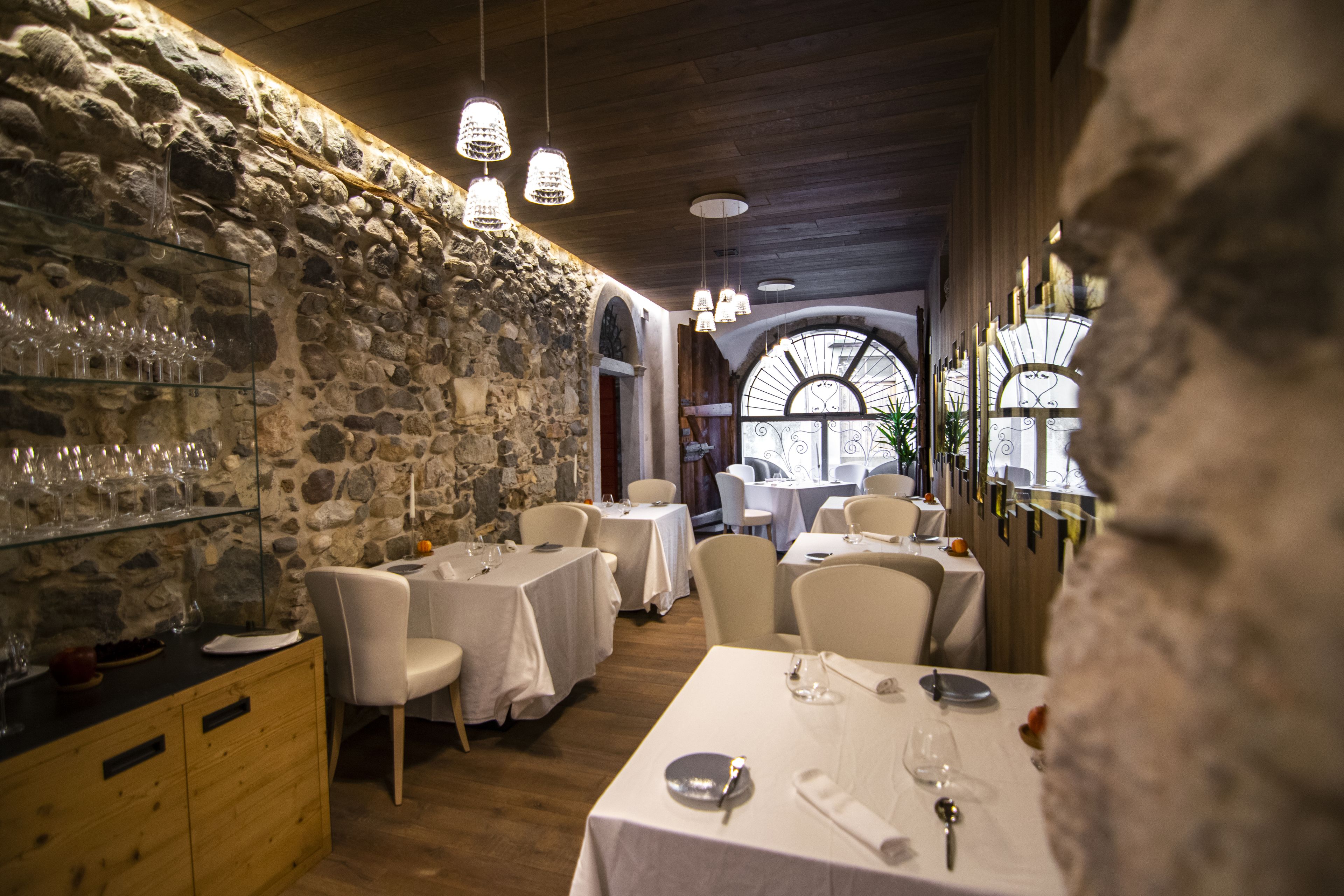 A restaurant with stone walls, white tables, and hanging lights.