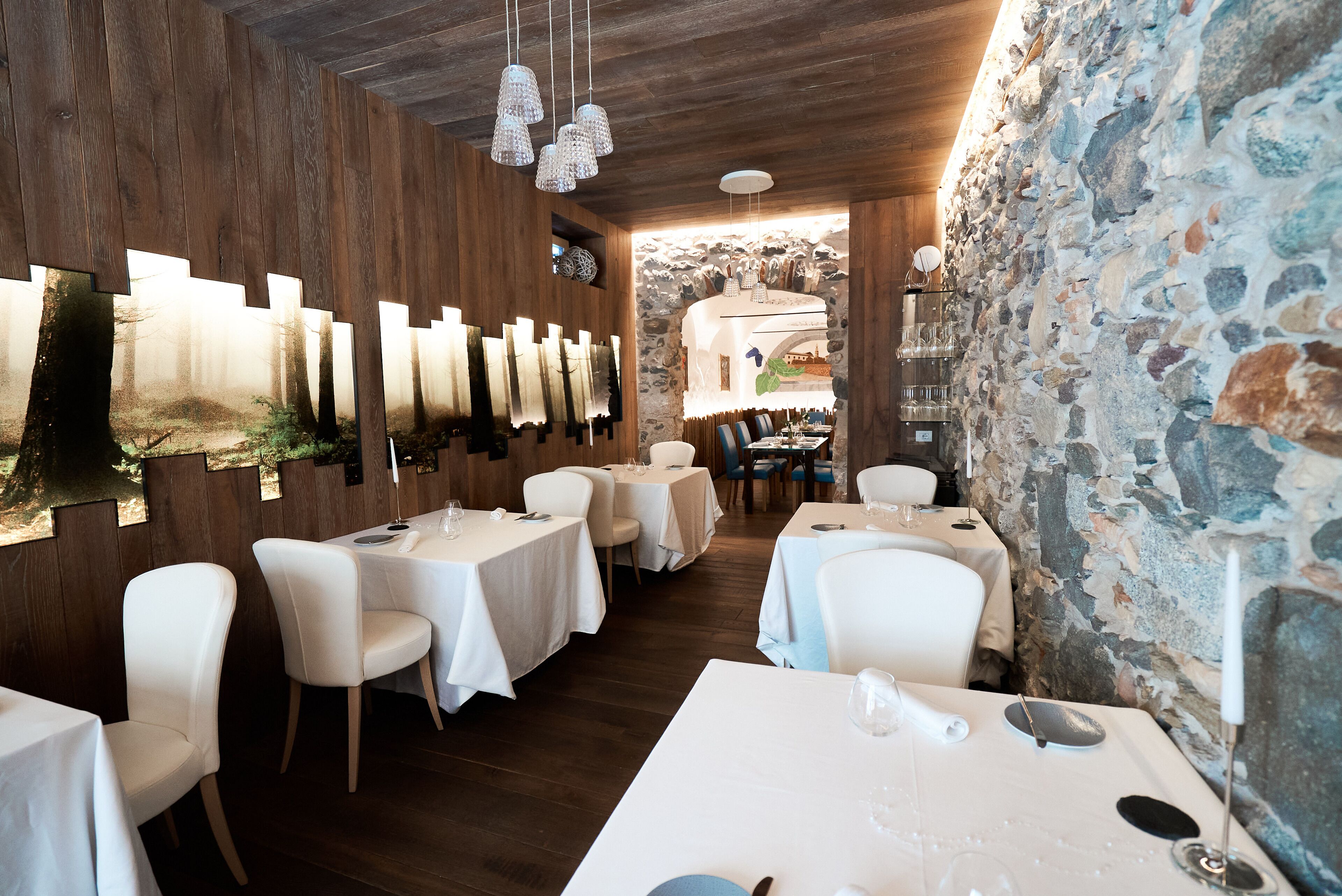 A restaurant with wooden walls, stone accents, and white tables and chairs.