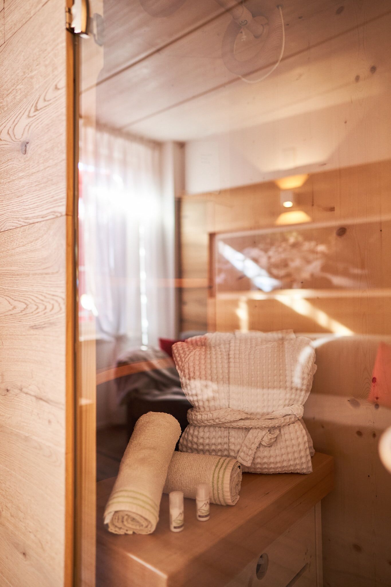 Interno di una baita in legno, con una panca di legno, asciugamani e un quadro appeso al muro.