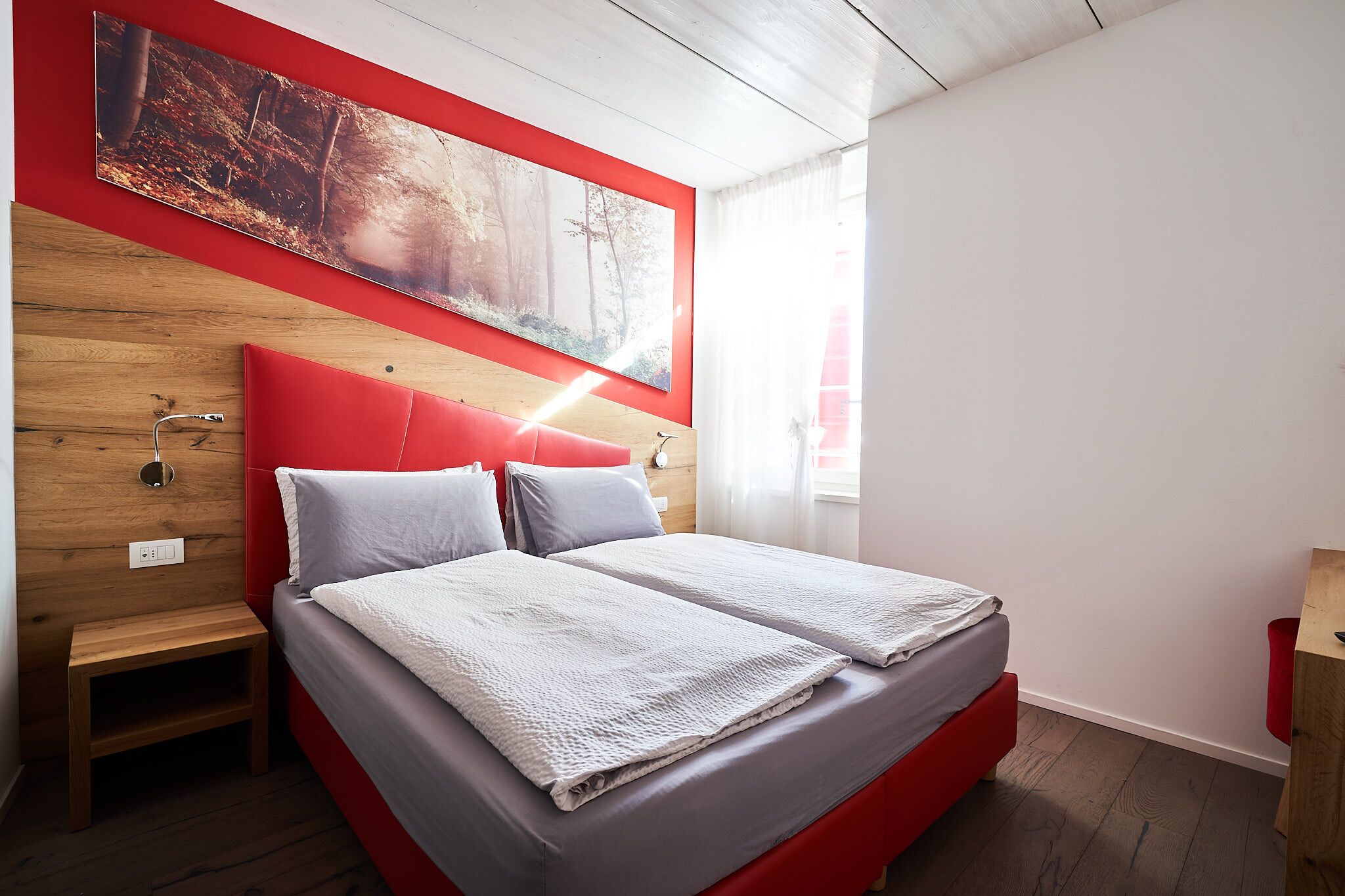 Ein modernes Schlafzimmer mit einem roten Kopfteil, einem großen Gemälde über dem Bett und einem kleinen Nachttisch.