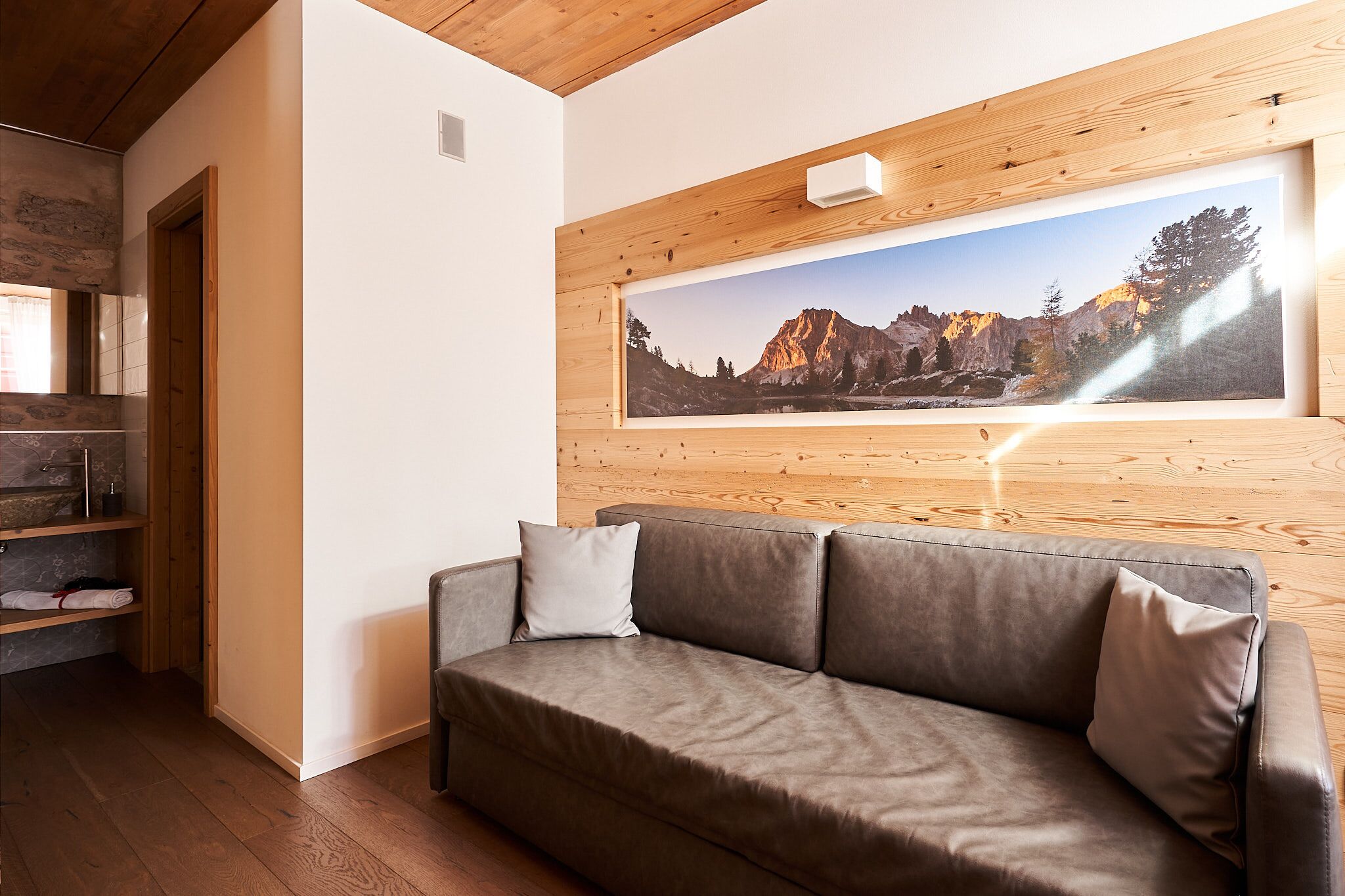 Una sala de estar moderna con techo de madera, un cuadro grande de paisaje enmarcado, un sofá de cuero marrón y piso de madera.