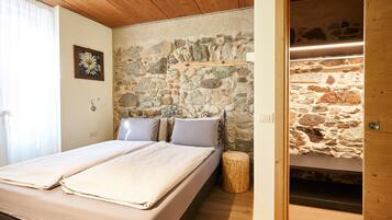 Ein Schlafzimmer mit einer Steinswand, einem Bett mit zwei Kissen, Holzboden und einem kleinen Holzschemel.