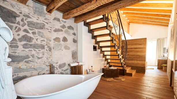 A modern bathroom with a freestanding bathtub, a stone wall, and a wooden staircase. - La Filanda Relax & Gourmet (Denno)