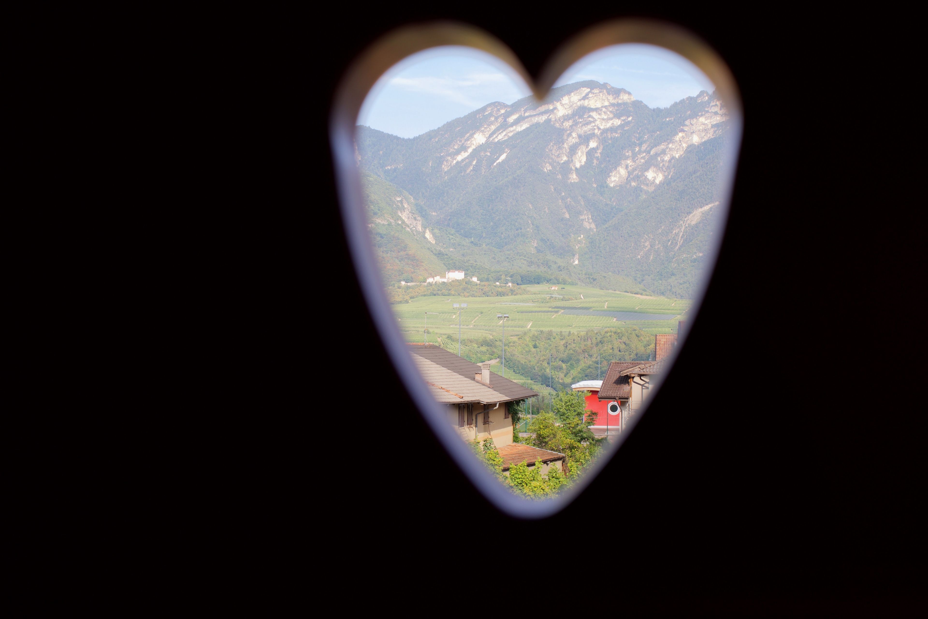 A heart-shaped window view of a mountain landscape with buildings.