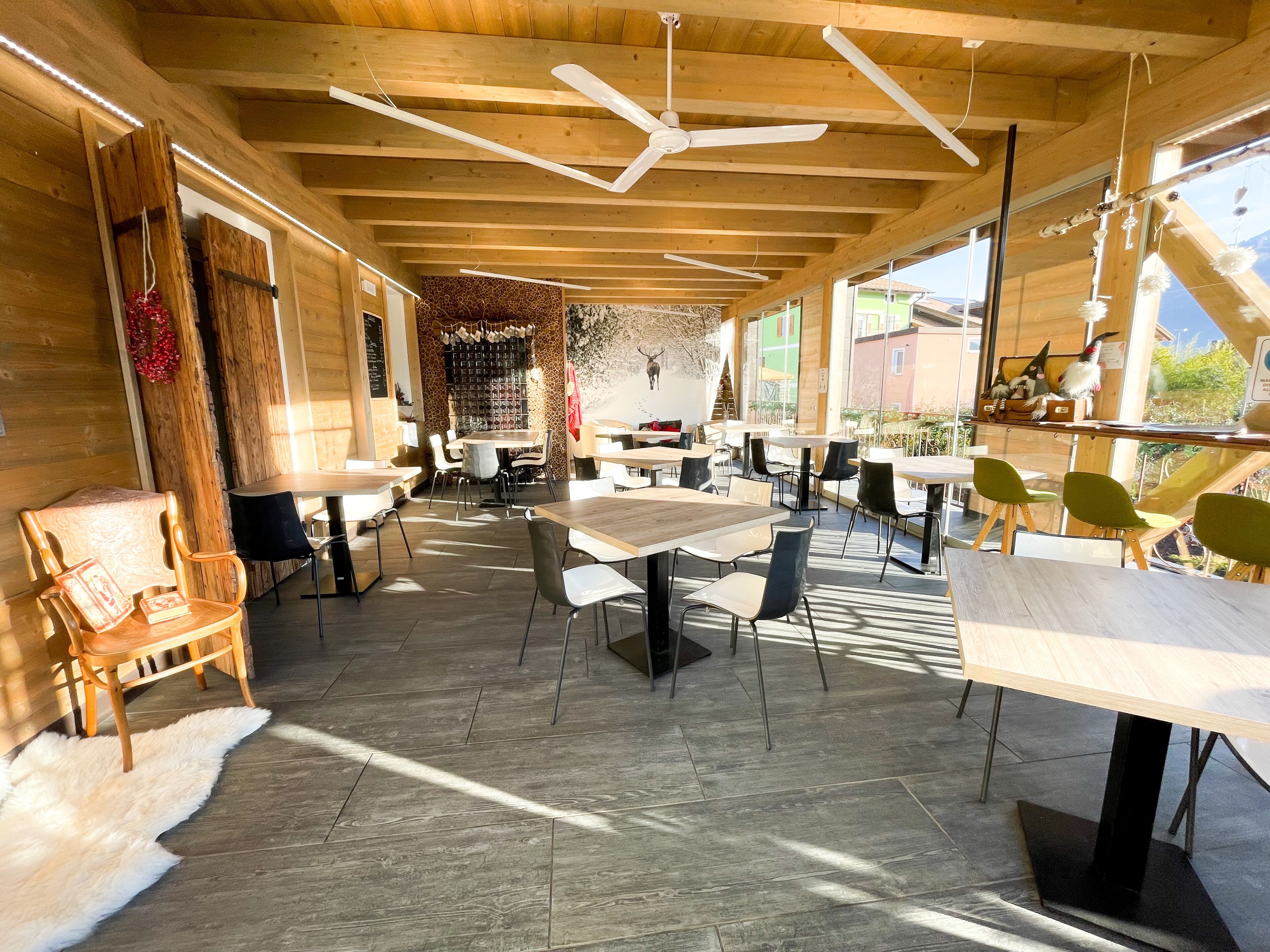 Un vaste espace intérieur doté de poutres en bois, de tables, de chaises et d’une grande fenêtre offrant une vue sur l’extérieur.