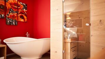 Un baño moderno con una bañera independiente, una pared roja y un mueble de madera con toallas.