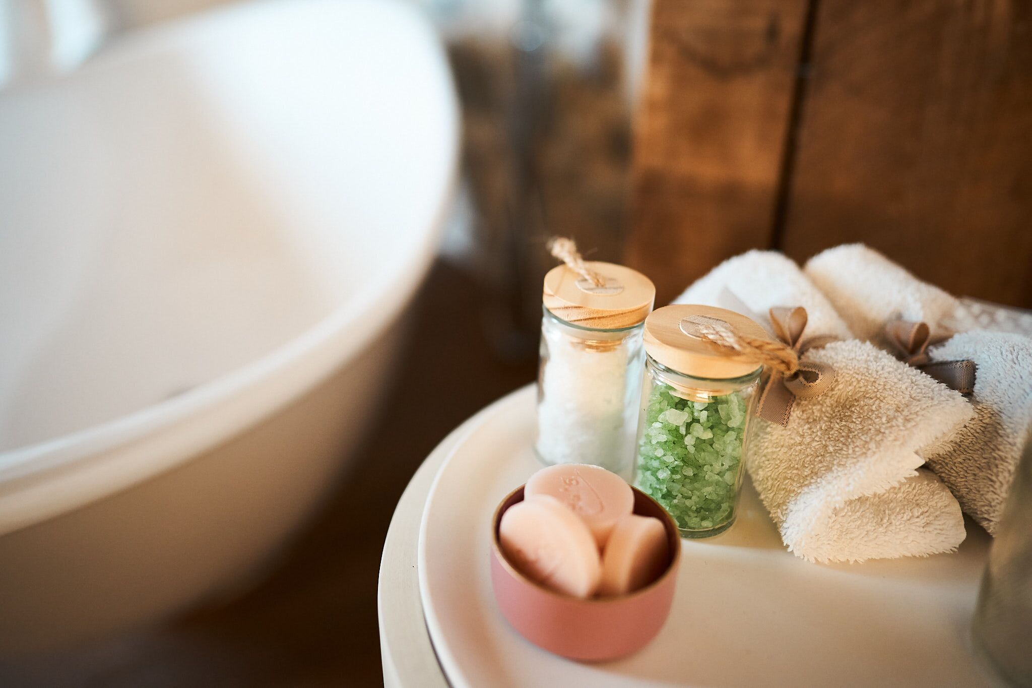 Un tocador de baño con un lavabo blanco, un cuenco pequeño rosa con jabón, dos frascos de vidrio con tapas y una toalla.