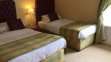 A hotel room with two beds, a nightstand, a lamp, and a window with curtains.