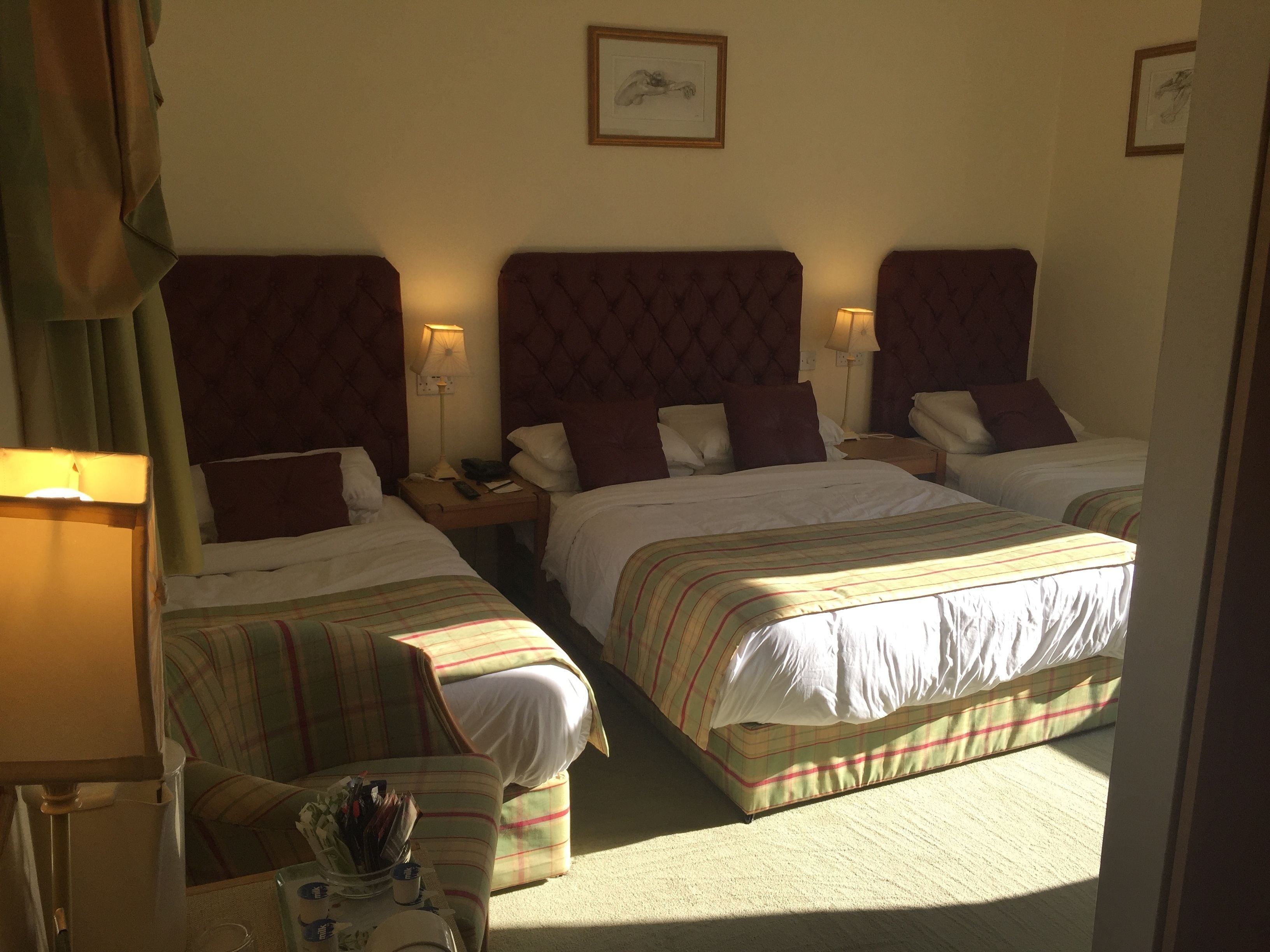A hotel room with two beds, a nightstand, a lamp, and a chair.