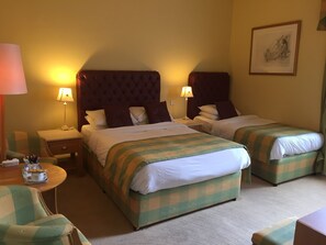 A hotel room with two beds, each with a checkered bedspread, a tufted headboard, and bedside lamps. There is a small table with a tray of breakfast items, a chair, and a framed picture on the wall. - Faythe Guesthouse (Wexford)