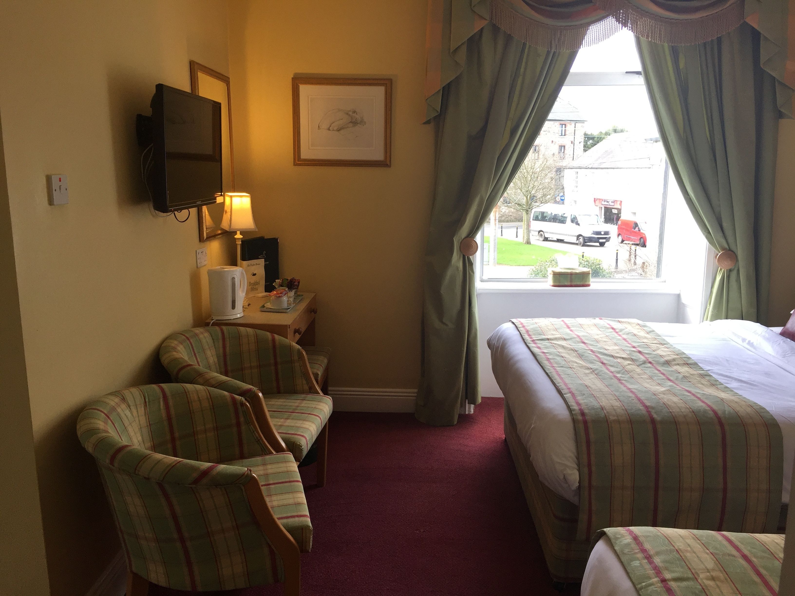 A hotel room with two beds, a television, a desk with a lamp, and a window with curtains.