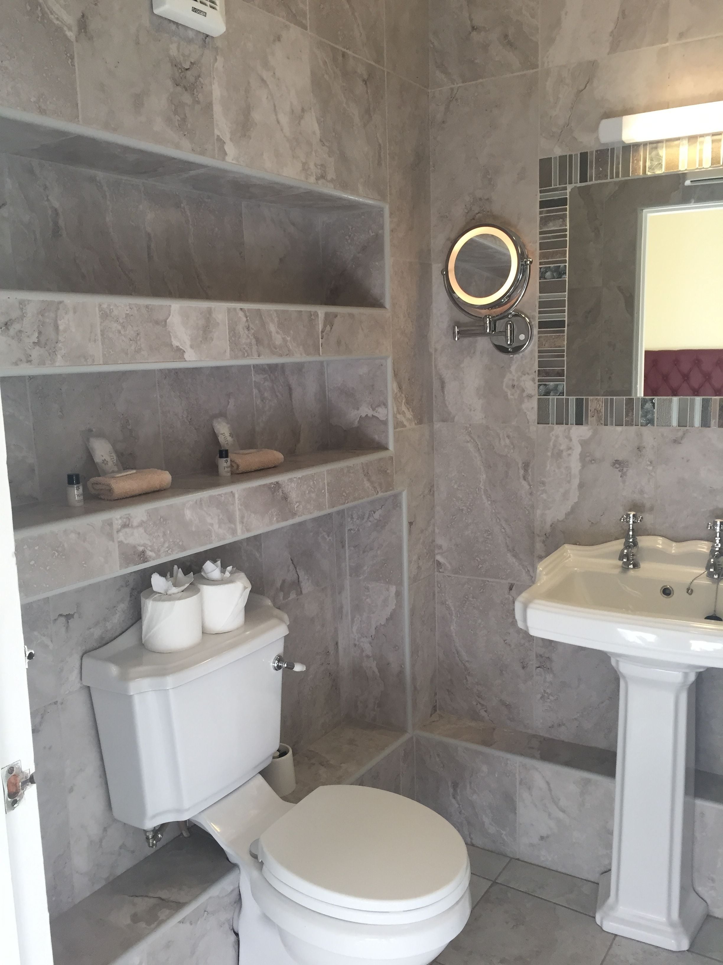 A bathroom with a toilet, shelves, a sink, and a mirror.