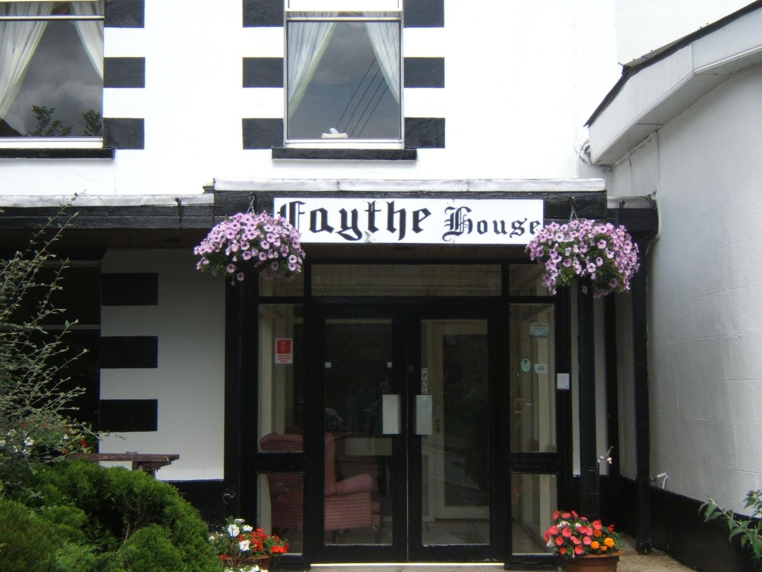 A building with a sign reading "Faythe House" above the entrance. There are hanging flower baskets above the door.