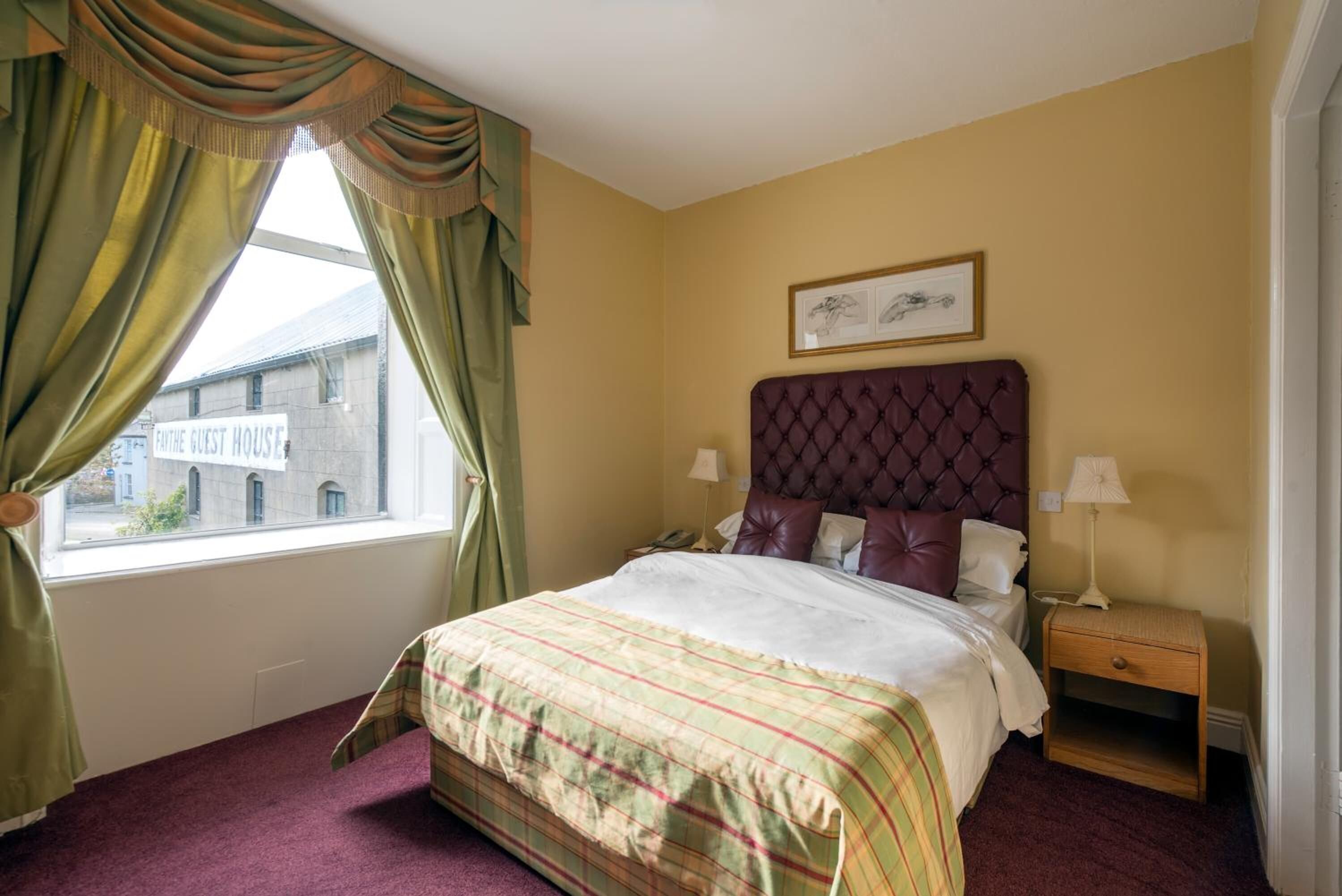 Un cuarto de hotel con una cama grande, una mesita de noche, una ventana con cortinas y un cuadro enmarcado en la pared.