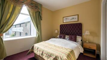Un cuarto de hotel con una cama grande, una mesita de noche, una ventana con cortinas y un cuadro enmarcado en la pared.