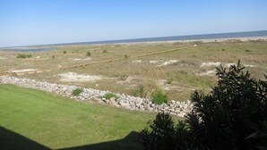 A coastal landscape with a grassy area, a wooden boardwalk, and a distant beach.