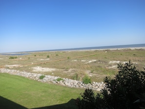 Een kustlandschap met een gazon, een houten looppad en een strand in de verte.
