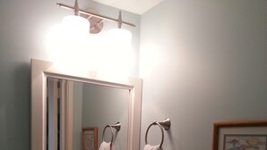 A bathroom with a sink, mirror, towel rings, and a framed picture on the wall.