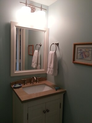 Een badkamer met een wastafel, spiegel, handdoekhouders en een ingelijste foto aan de muur.