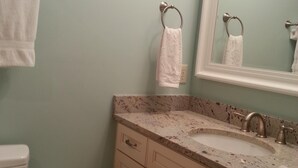 A bathroom with a toilet, sink, and mirror. There are towels hanging on the wall and a roll of toilet paper on the floor.