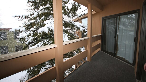 A covered balcony with a wooden railing, a sliding glass door, and a view of snow-covered trees. - Right in the Heart of Park City (Park City)