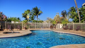 A swimming pool with a curved design, surrounded by a white fence and palm trees.