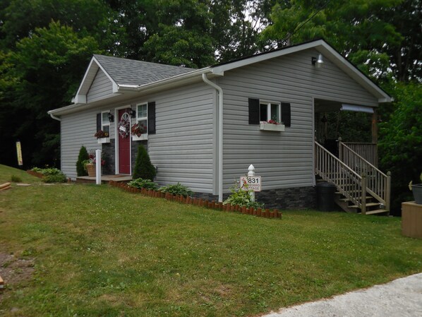 A single-story house with a red front door, a small porch with potted plants, a wooden staircase leading to a front door, and a mailbox.