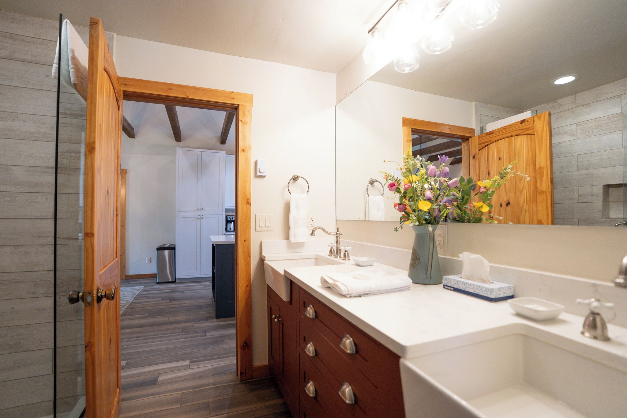 A modern bathroom with a wooden door, white vanity, and a large mirror.